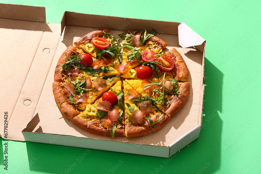 Cardboard box of delicious pizza with tomatoes and arugula on green background