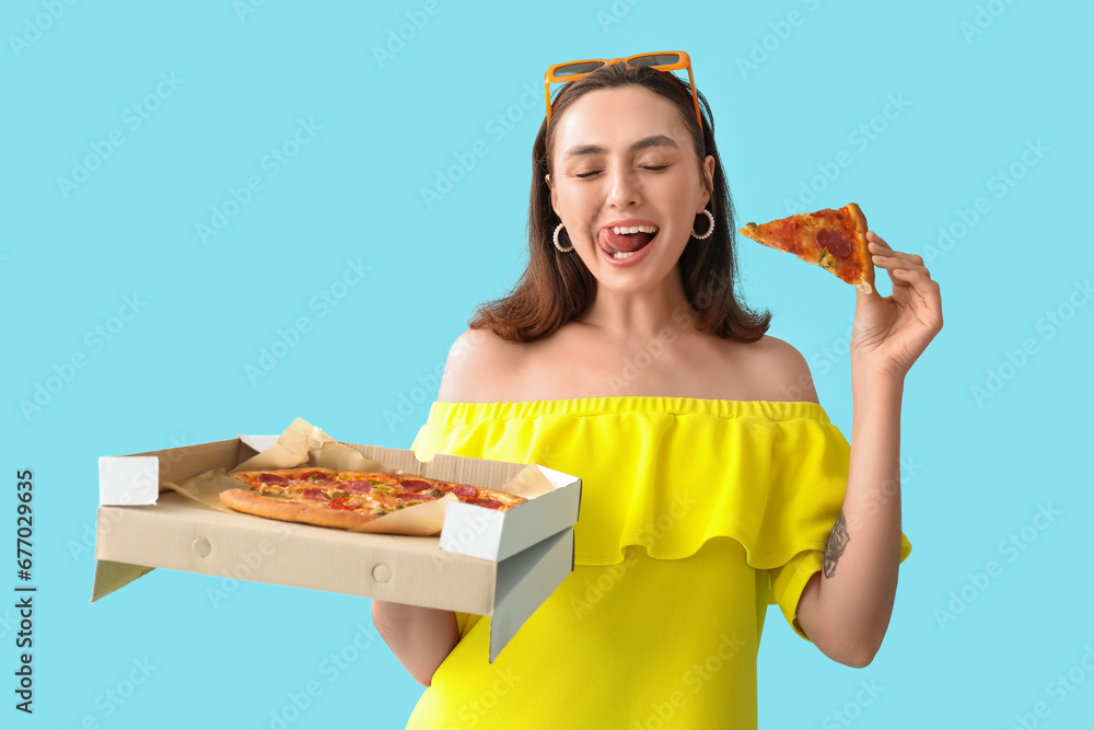 Young woman holding cardboard box with tasty pizza on blue background