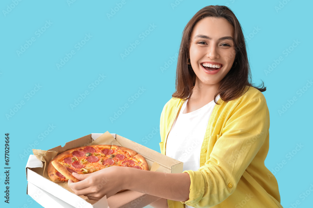 Young woman holding cardboard box with tasty pizza on blue background