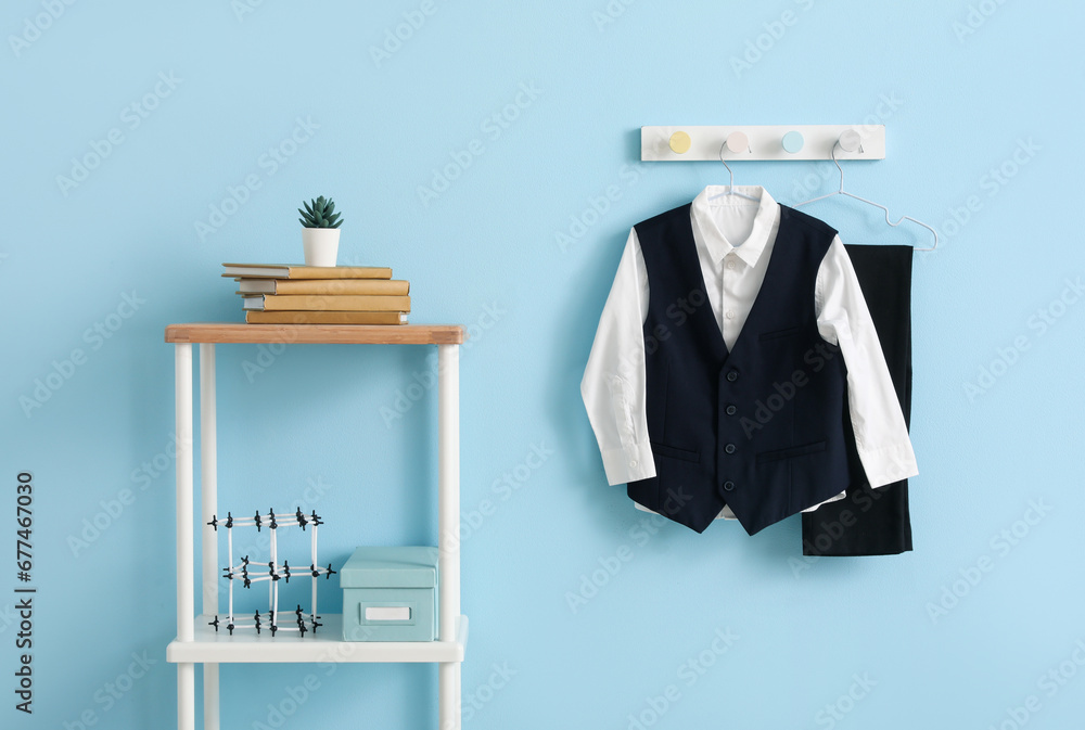 Shelving unit with books and stylish school uniform hanging on blue wall in room