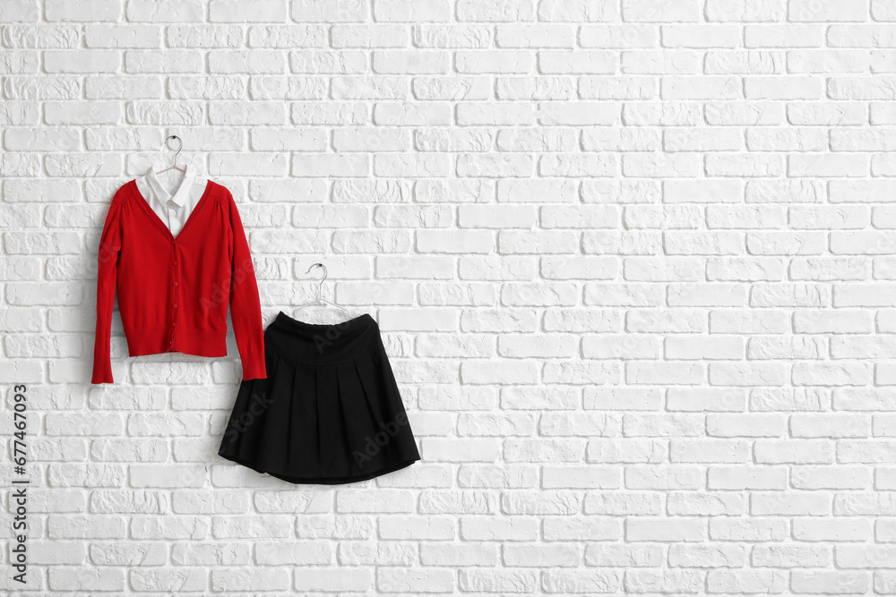 Stylish school uniform hanging on light brick wall in room