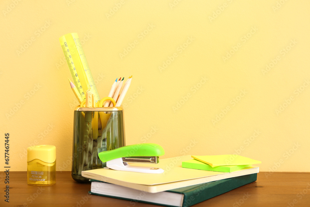 Holder with different stationery and notebooks on wooden desk, closeup