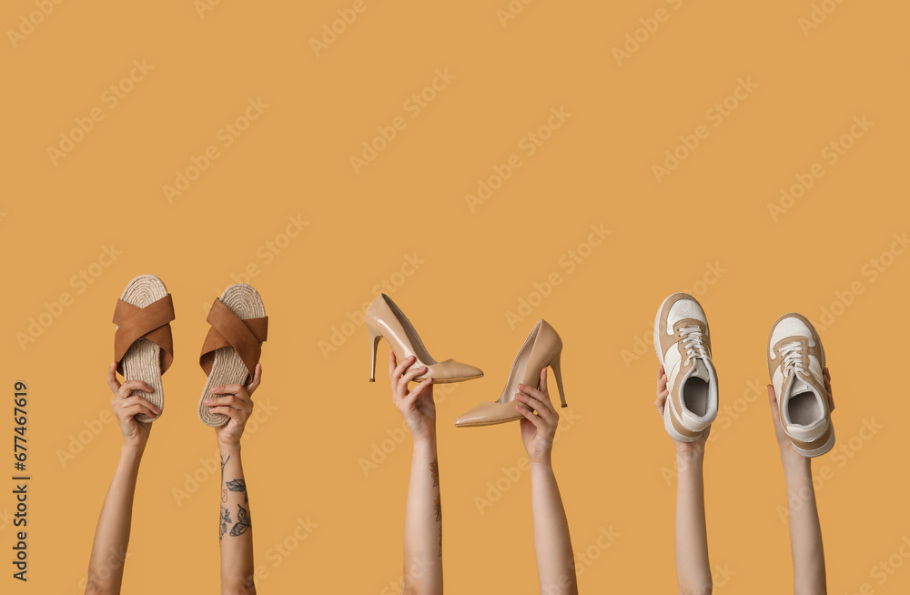 Women holding different stylish shoes on yellow background