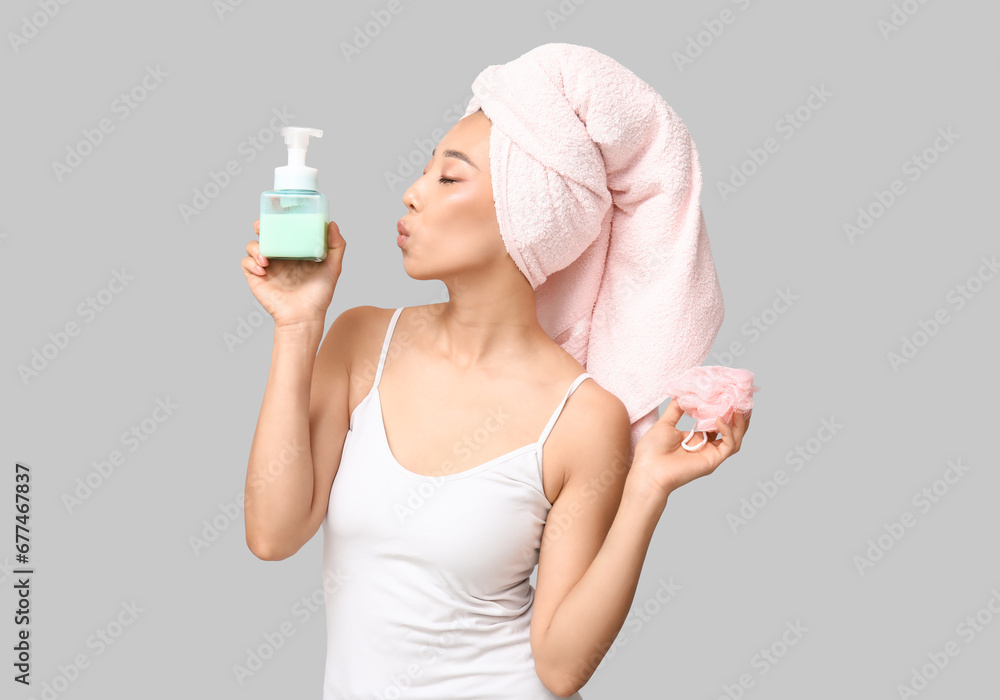 Young Asian woman with shower gel and loofah blowing kiss on light background