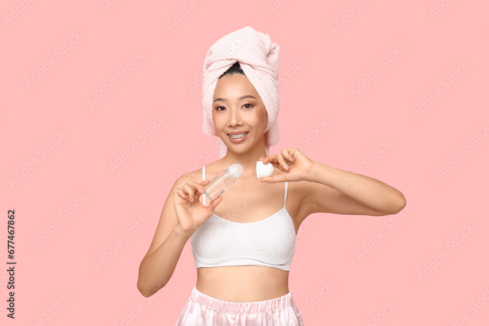 Young Asian woman with roll-on deodorant on pink background