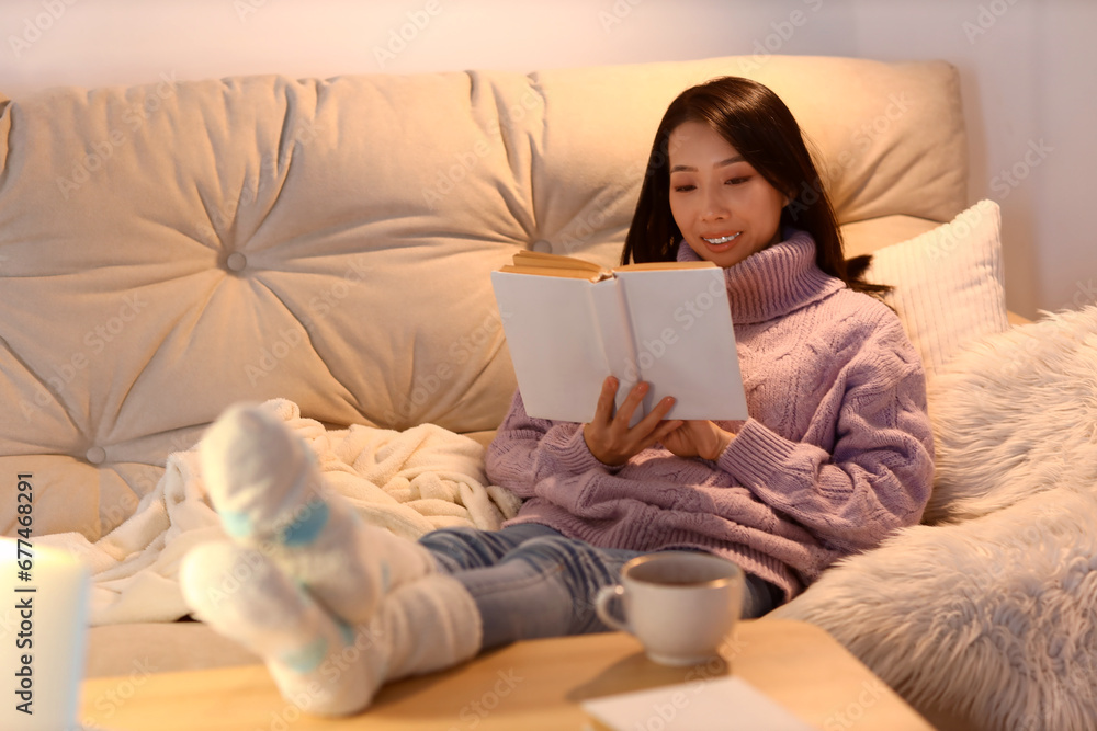 Young Asian woman reading book at home in evening