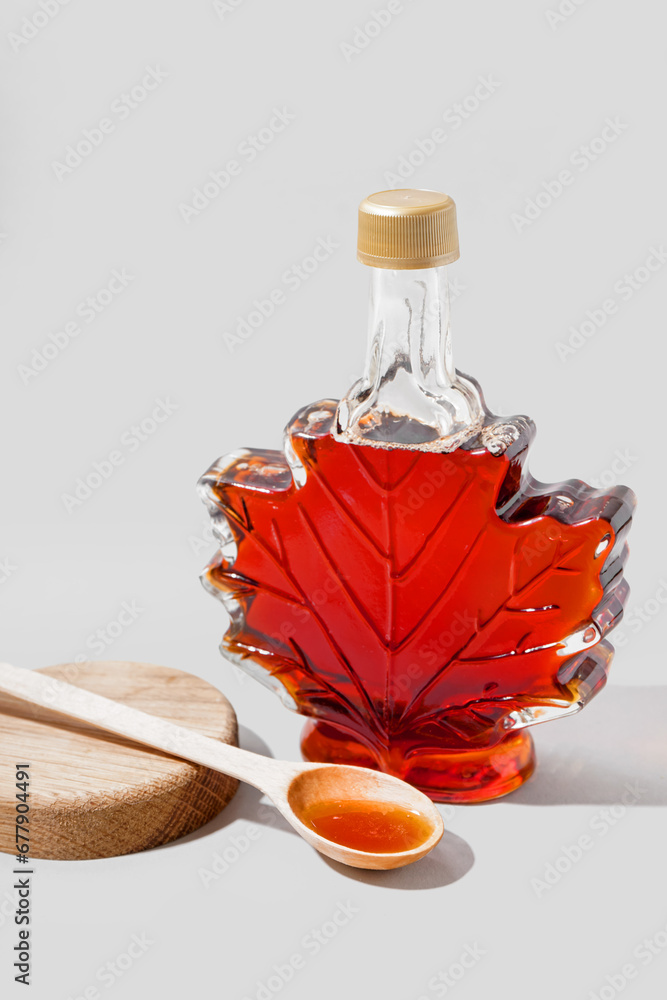 Bottle and spoon of tasty maple syrup on grey background