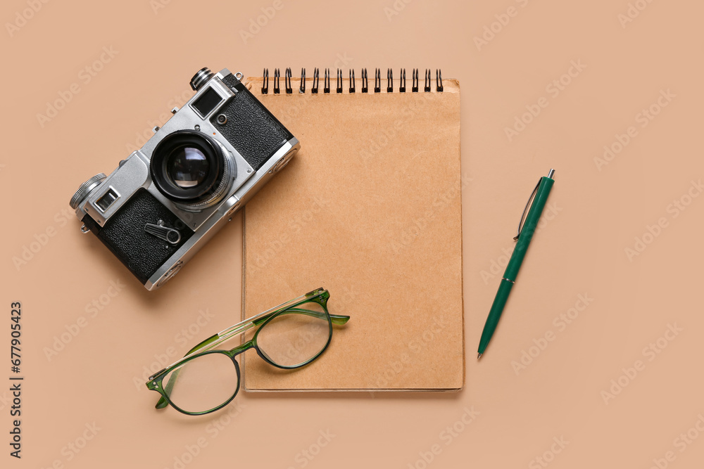 Notebook with pen, photo camera and eyeglasses on beige background