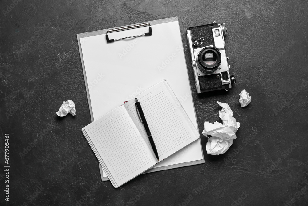 Notebook with clipboard, photo camera and crumpled paper on dark background