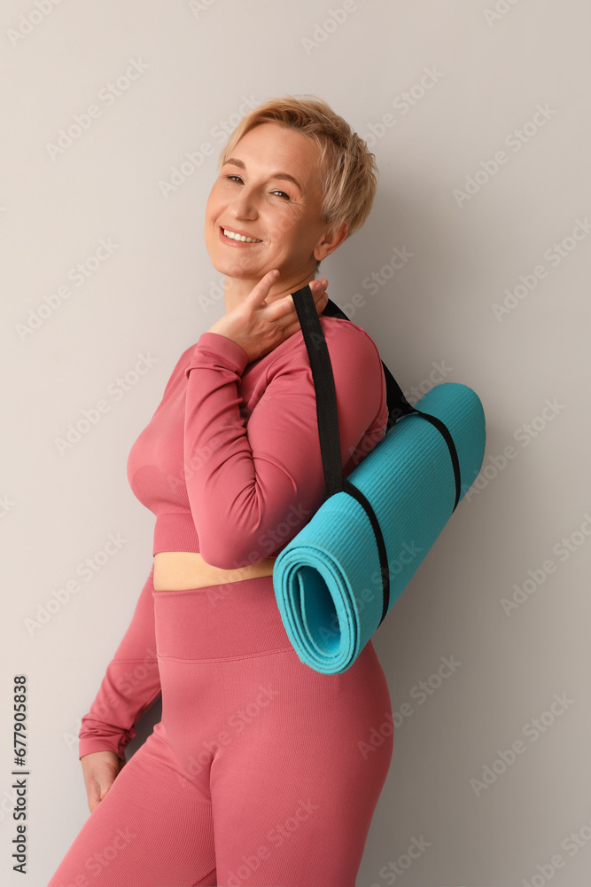 Mature woman with yoga mat on light background