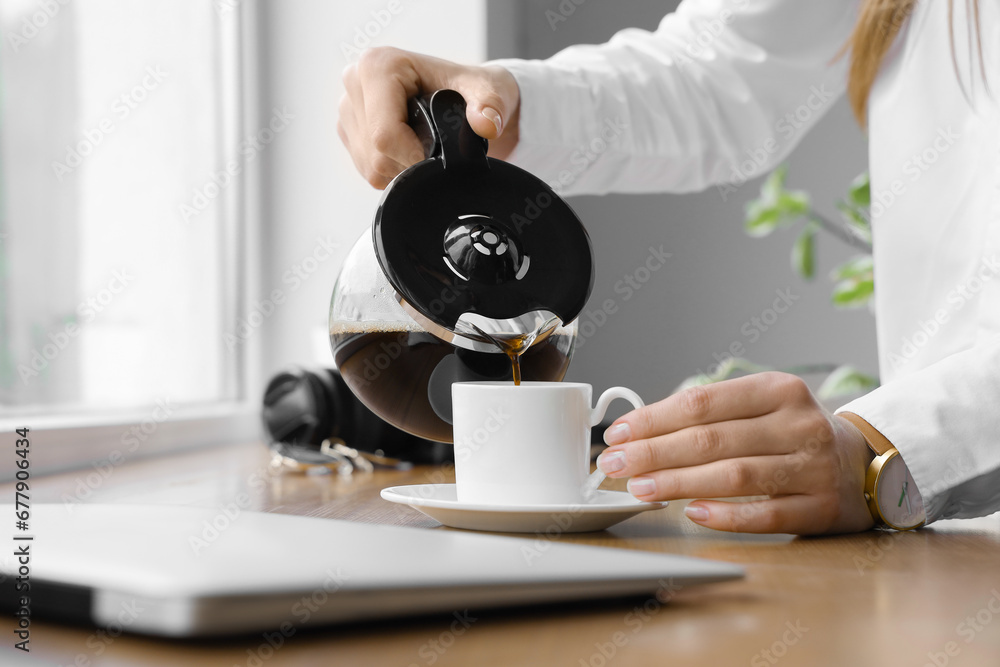 Woman pouring coffee from pot into cup on wooden windowsill