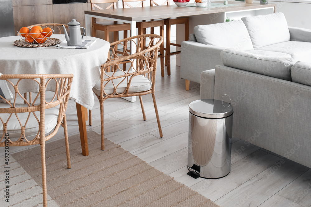 Metallic trash bin near sofa in interior of modern kitchen