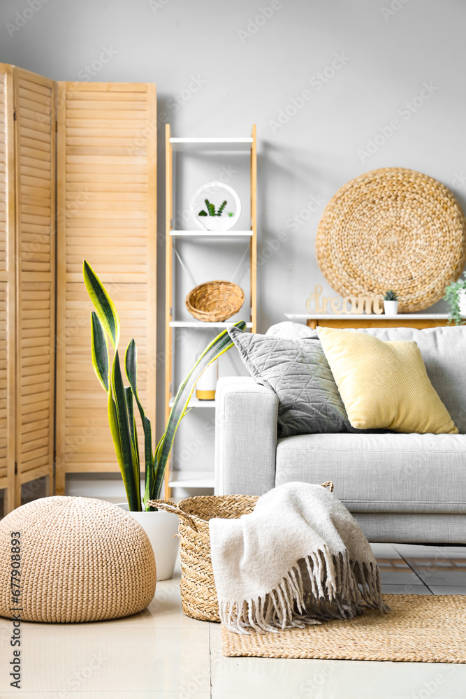 Cozy grey sofa and basket with soft blanket in interior of light living room