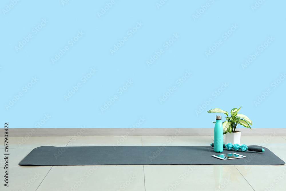 Tablet computer with bottle, massage roller and plant on fitness mat in gym