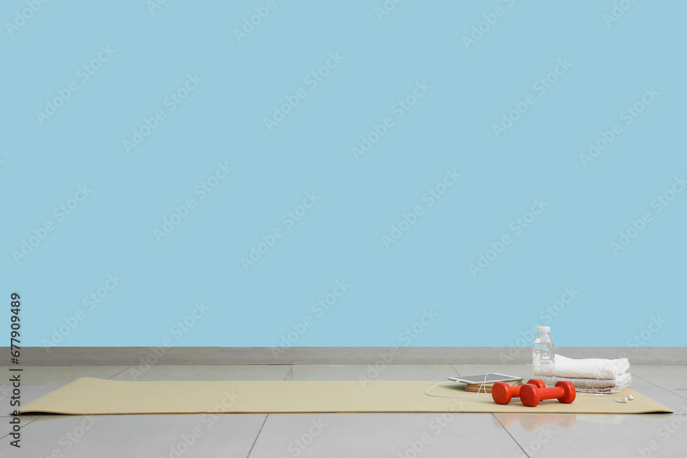 Tablet computer with dumbbells, bottle of water and towels on fitness mat in gym