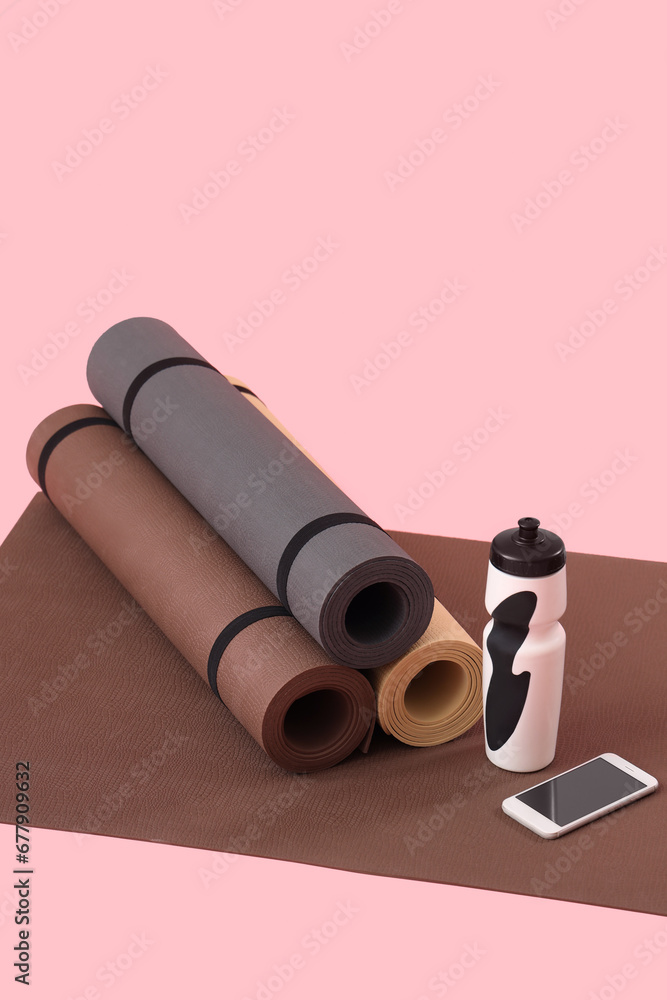 Fitness mats with bottle and mobile phone on pink background