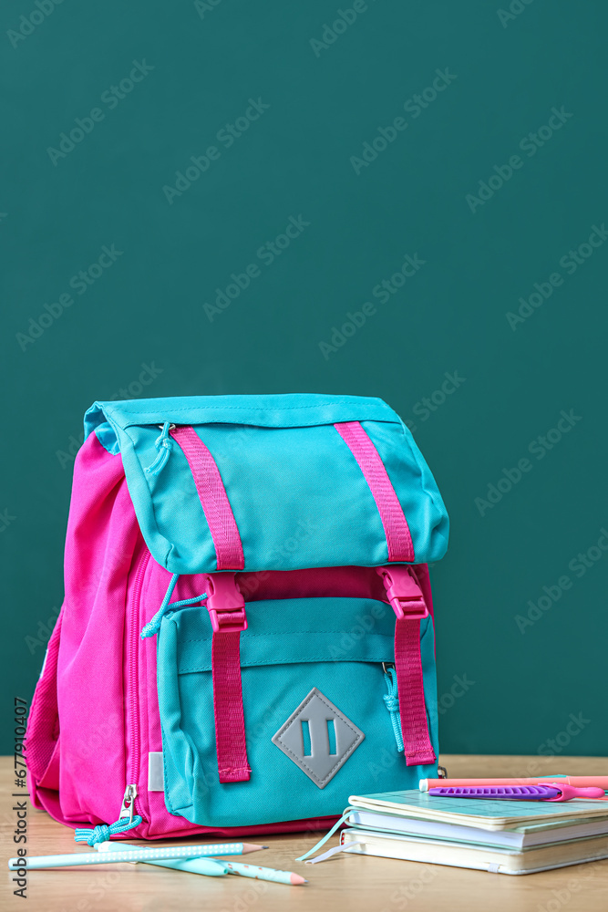 Colorful school backpack with stationery on brown wooden table near green chalkboard