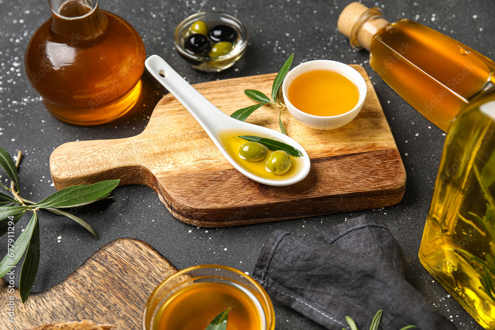 Bowls, spoon, bottles and jug of fresh olive oil on black background