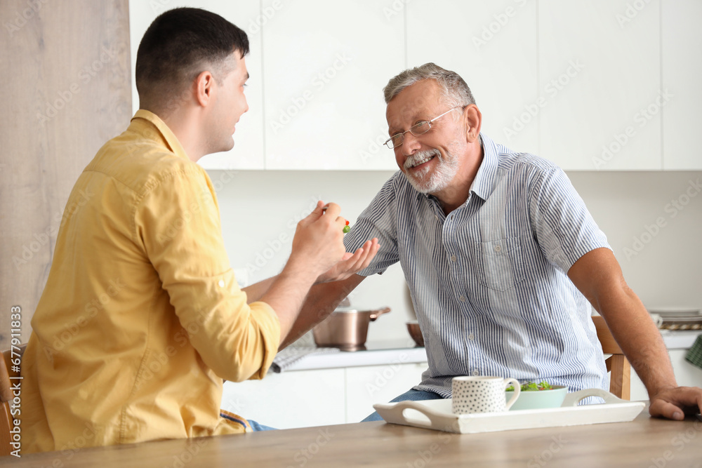 Young man feeding his father in kitchen