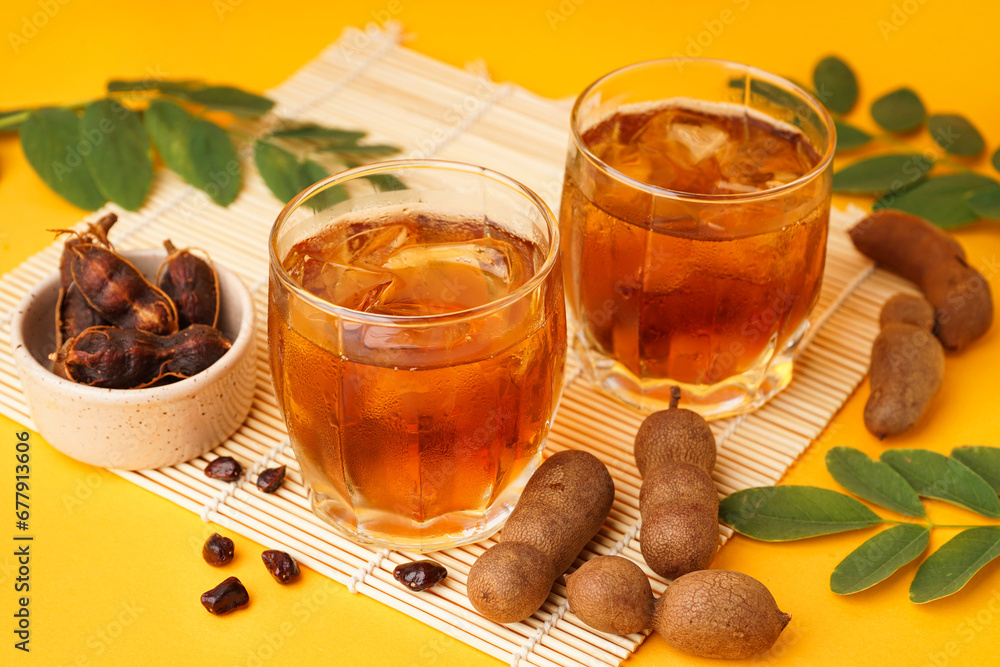 Glasses of tasty tamarind drink and fruits on yellow background