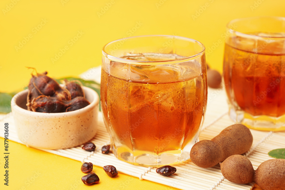 Glasses of tasty tamarind drink and fruits on yellow background