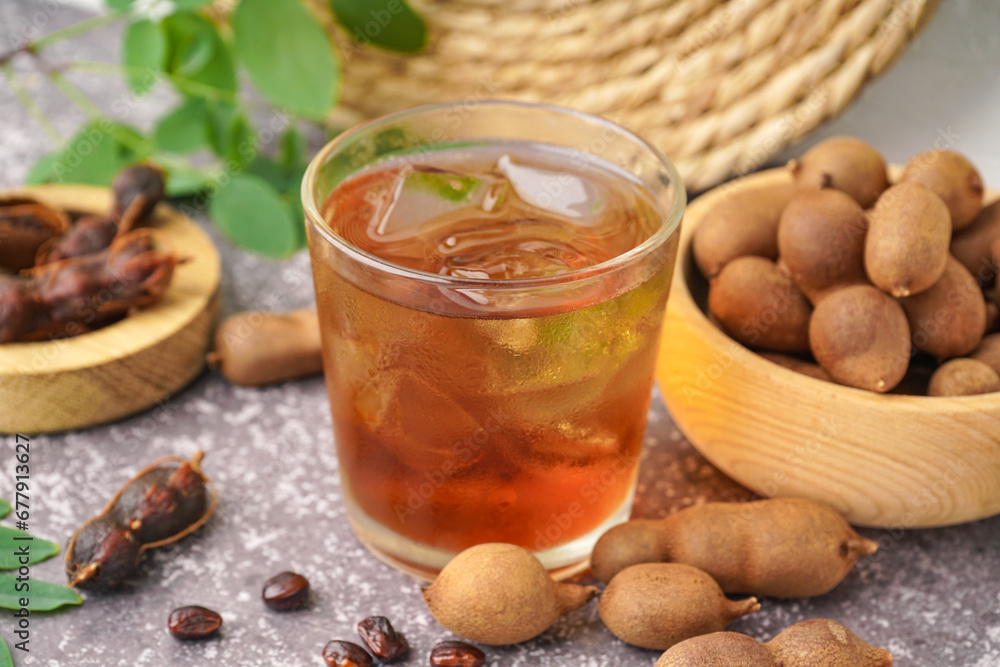 Glass of tasty tamarind drink and fruits on grey background