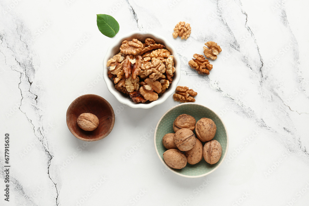 Bowls of tasty walnuts on white marble background