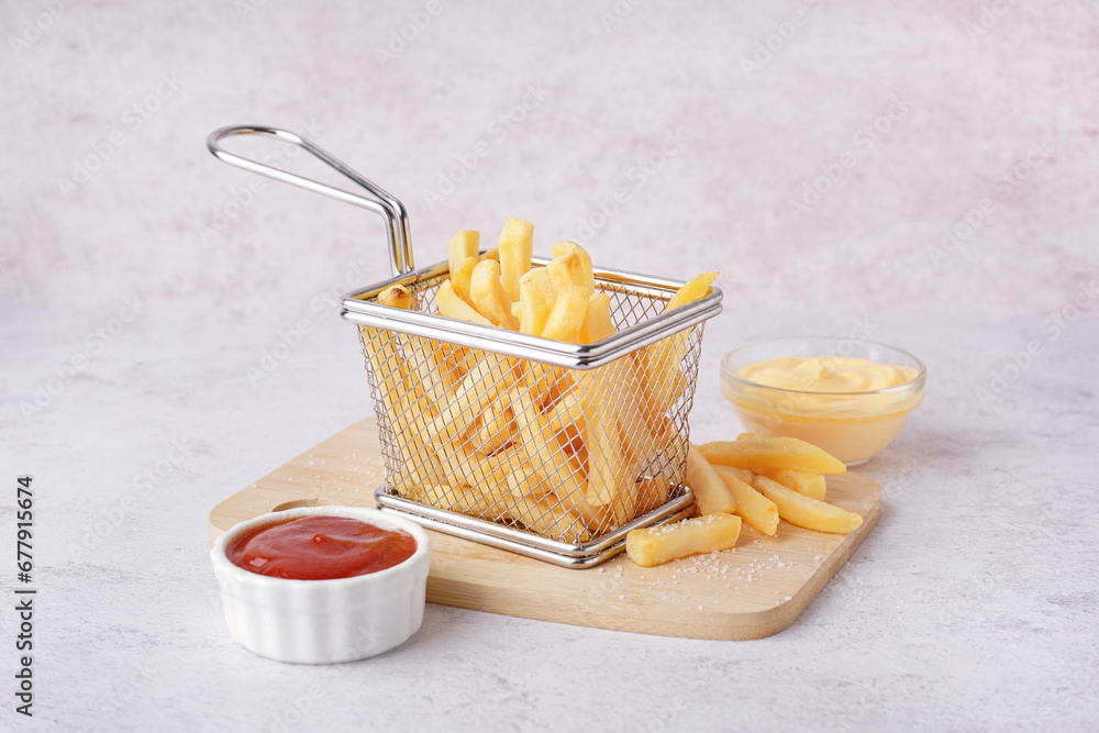 Deep fryer basket with tasty french fries and sauces on white background