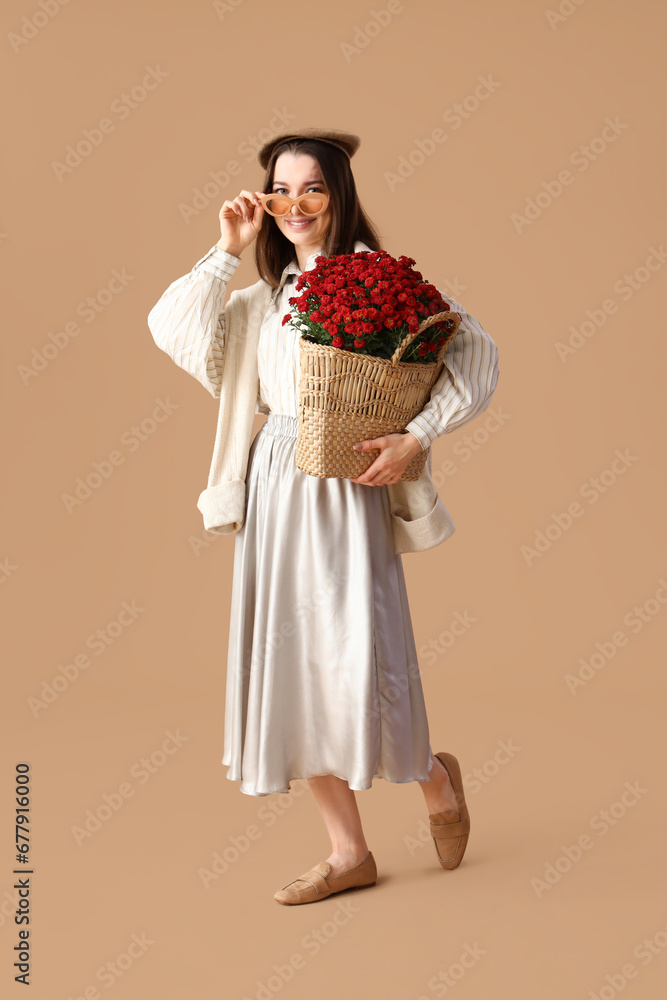 Young woman with chrysanthemum flowers on beige background