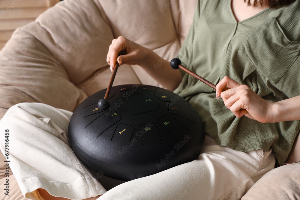 Young woman with sticks playing glucophone in armchair at home, closeup