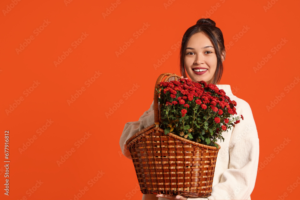 Young Asian woman with chrysanthemum flowers on orange background