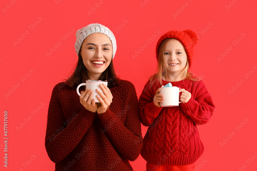 Happy young mother and her little daughter with mugs of hot chocolate on red background