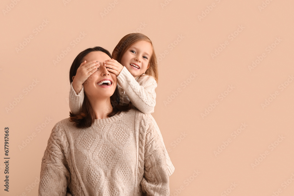 Little daughter covering eyes of her mother on beige background