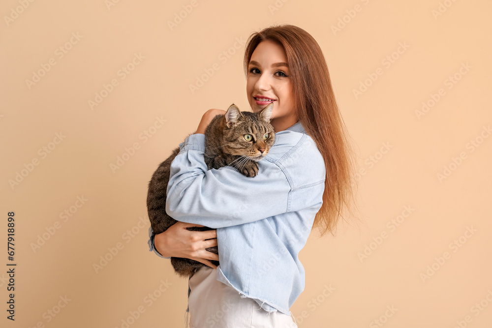 Pretty young woman with cute tabby cat on beige background