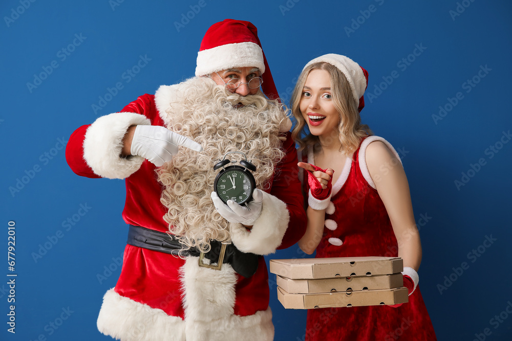 People dressed as Santa Claus with pizza boxes pointing at alarm clock on blue background