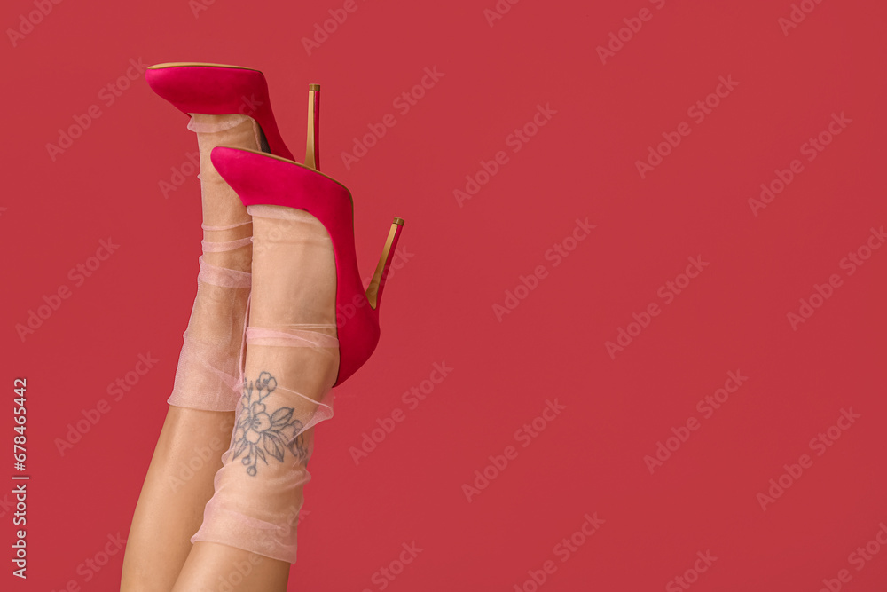 Tattooed female legs in heels on pink background, closeup