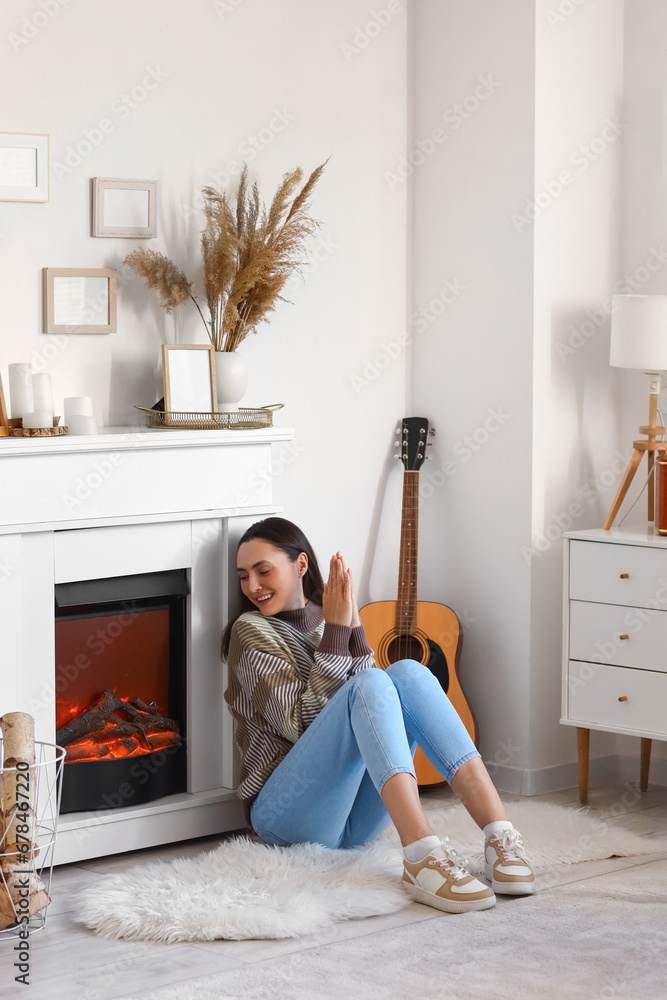 Frozen young woman warming near fireplace at home