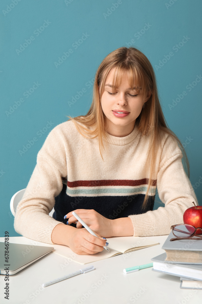 Female student doing homework at table on blue background