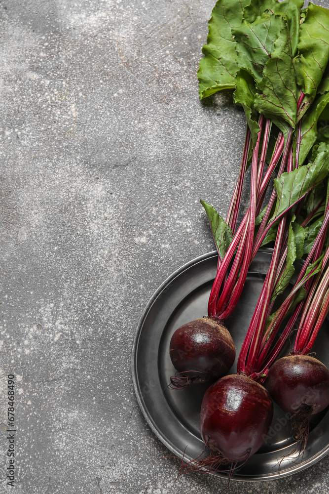 Plate of fresh beets with green leaves on grey background