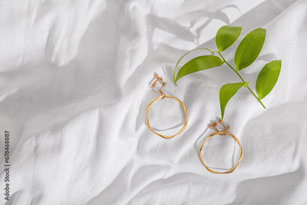 Beautiful golden earrings with plant leaves on white cloth