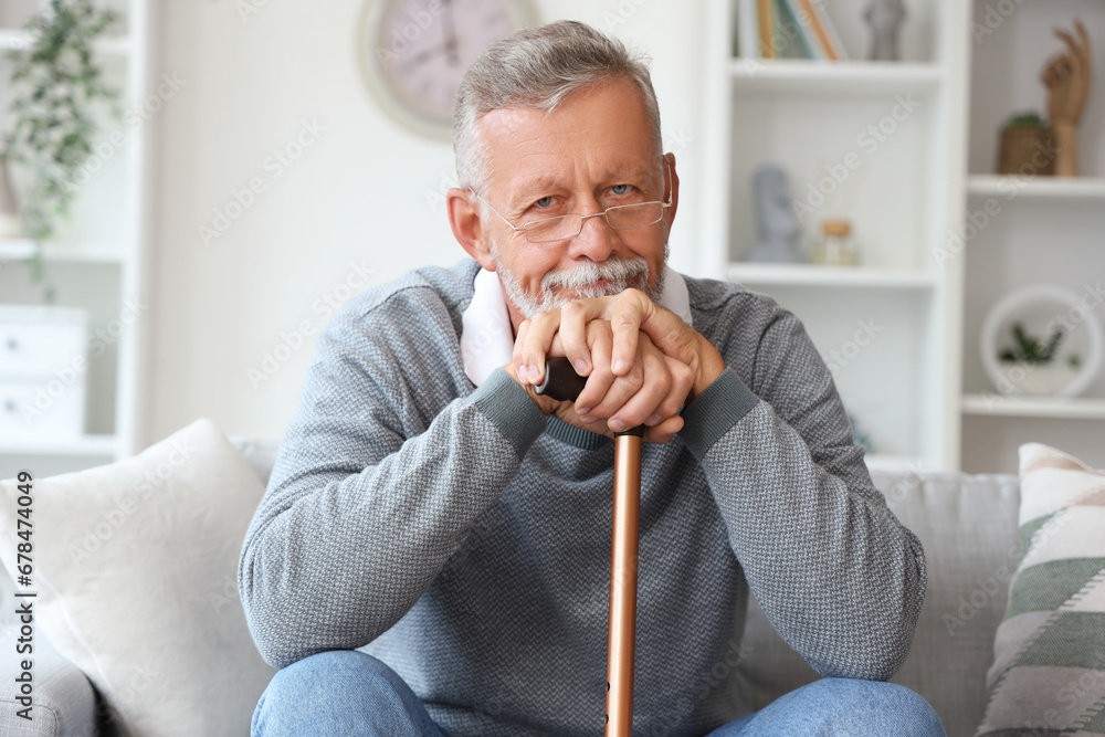 Senior man with stick sitting on sofa at home