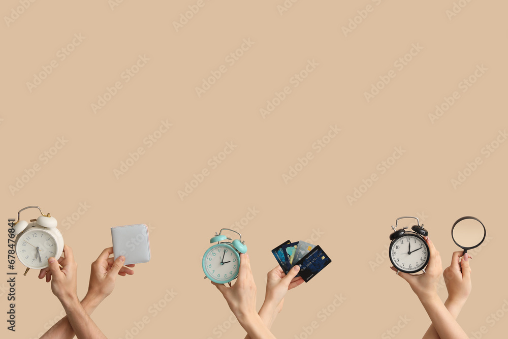 Hands holding alarm clocks, credit cards and magnifier on beige background