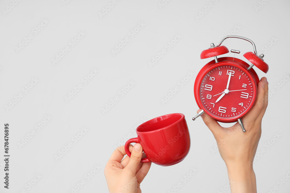 Female hands holding alarm clock and cup on grey background