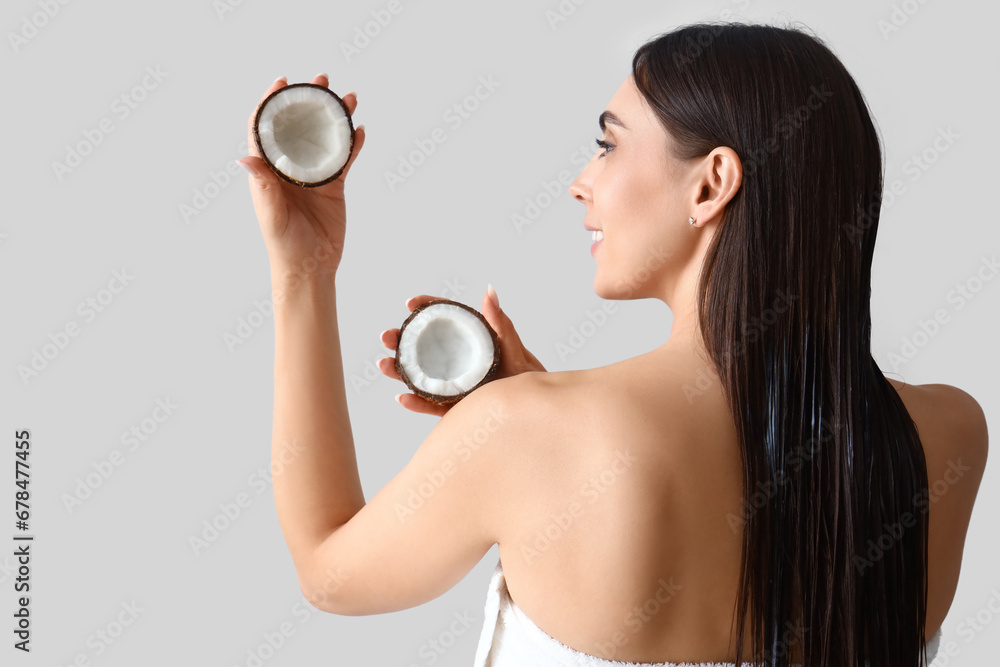 Beautiful young woman with coconut on light background, back view