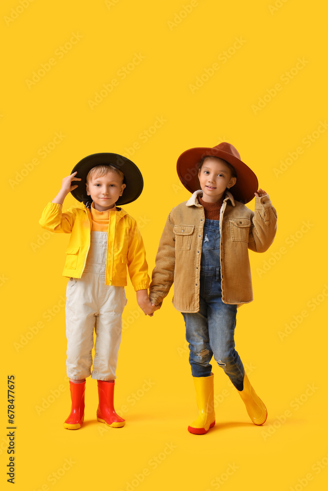 Little children in rubber boots holding hands on yellow background