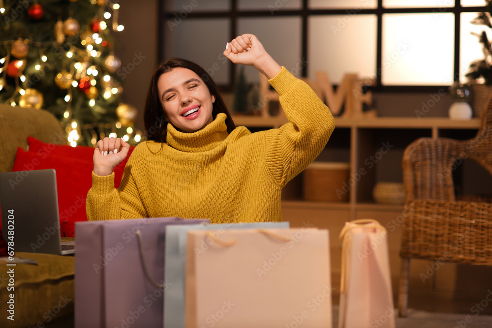 Happy young woman with shopping bags at home on Christmas eve