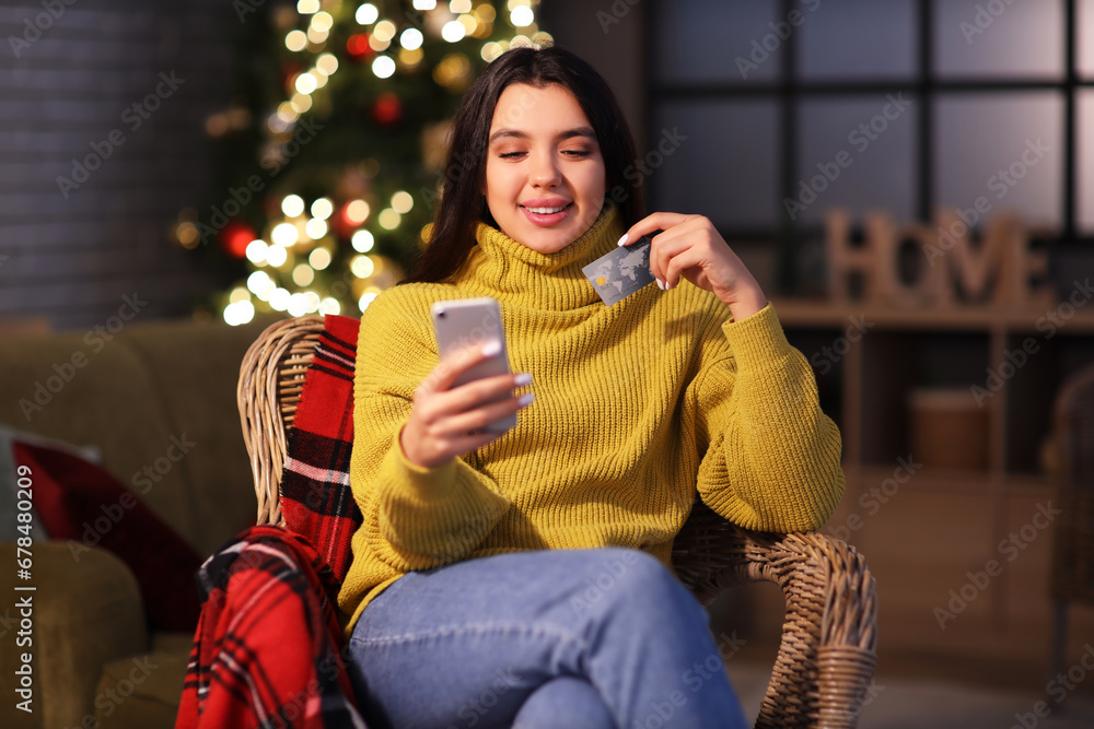 Young woman with mobile phone and credit card shopping online for Christmas at home