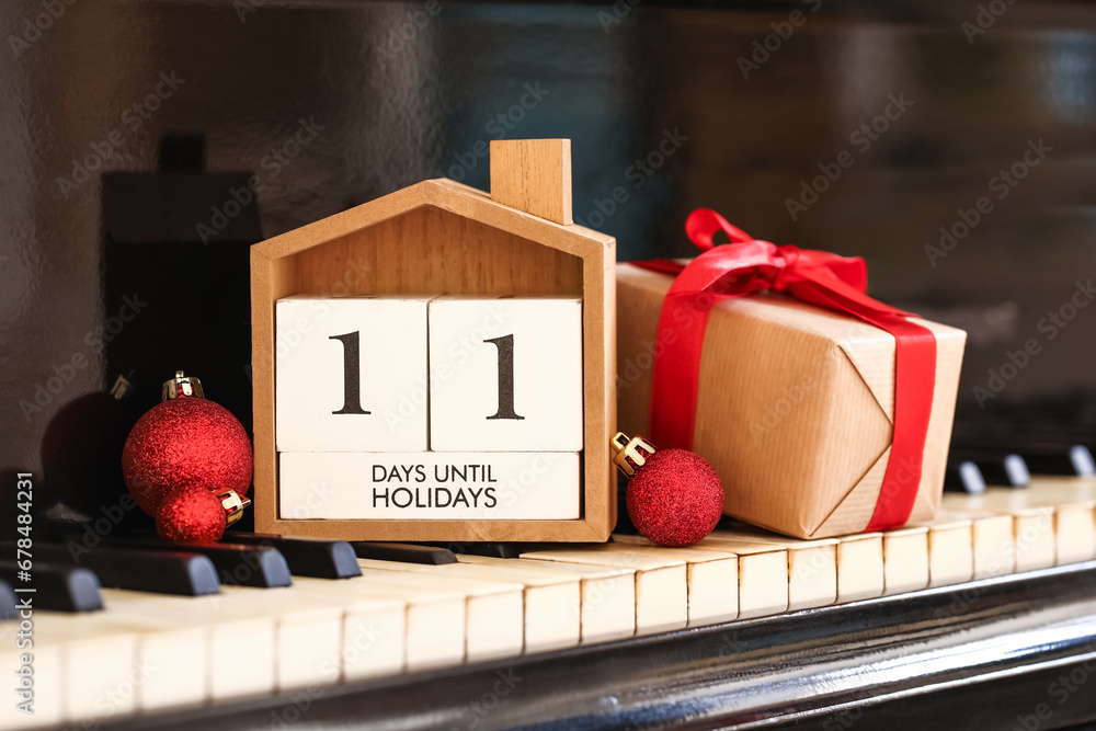 Calendar with text 11 DAYS UNTIL HOLIDAYS, Christmas gift and balls on piano keys