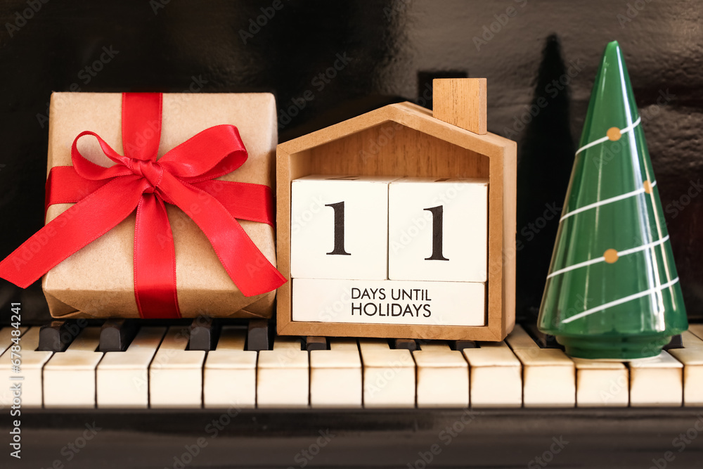 Calendar with text 11 DAYS UNTIL HOLIDAYS, Christmas gift and decor on piano keys, closeup