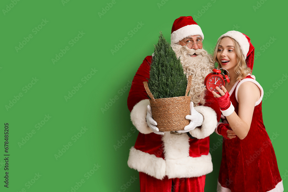 People dressed as Santa Claus with alarm clock and Cypress tree on green background